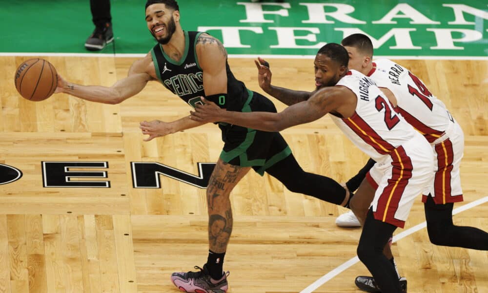 This action-packed image captures a dynamic moment during a basketball game, featuring a player from the Boston Celtics driving towards the basket with the ball, while defenders from the Miami Heat try to block his path. The Celtics player, wearing a green jersey with the number 0, exhibits skillful control and determination as he maneuvers around his opponents. The intense focus and physicality of the players are vividly displayed against the backdrop of the vibrant court, adding to the excitement of the match.