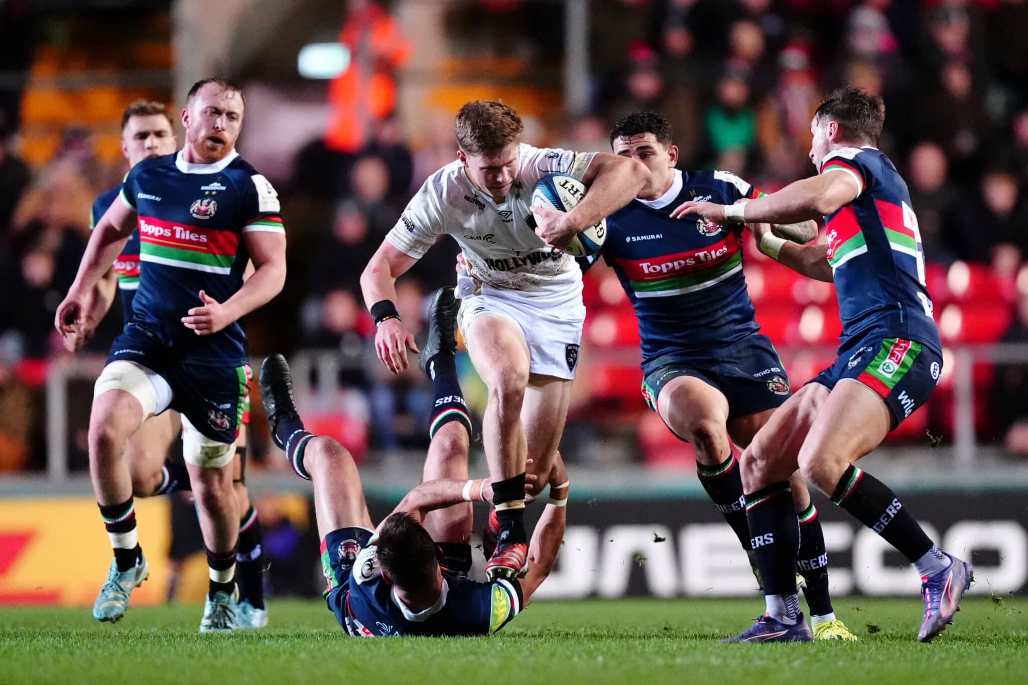 Intense rugby action with players from opposing teams tackling fiercely during a night game.