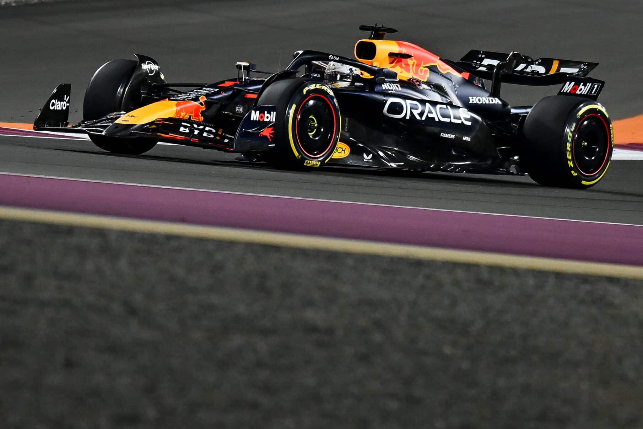 ed Bull Racing Formula One car, painted black with yellow and red accents, races along a track during a night race, with illuminated track boundaries enhancing the high-speed scene.