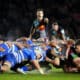 Intense rugby match scene with a scrum half poised to release the ball from the scrum, under the watchful eyes of competitors.