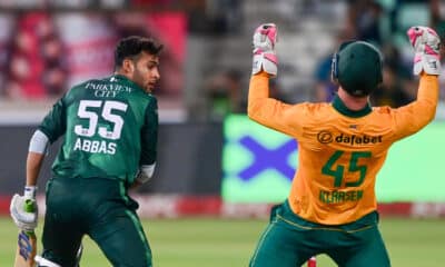 The image shows a moment from a cricket match with a batsman and a wicketkeeper in action. The batsman, dressed in a green jersey labeled "Abbas" and the number 55, is likely in the process of taking a run or reacting to a play. The wicketkeeper, in a vibrant orange kit with the number 45, is energetically raising his glove, possibly celebrating a dismissal or directing his teammates. The scene captures the intensity and excitement typical of a cricket game, highlighting player interactions and vibrant team colors.