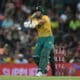 A South African cricketer in action, striking the ball during a night match.